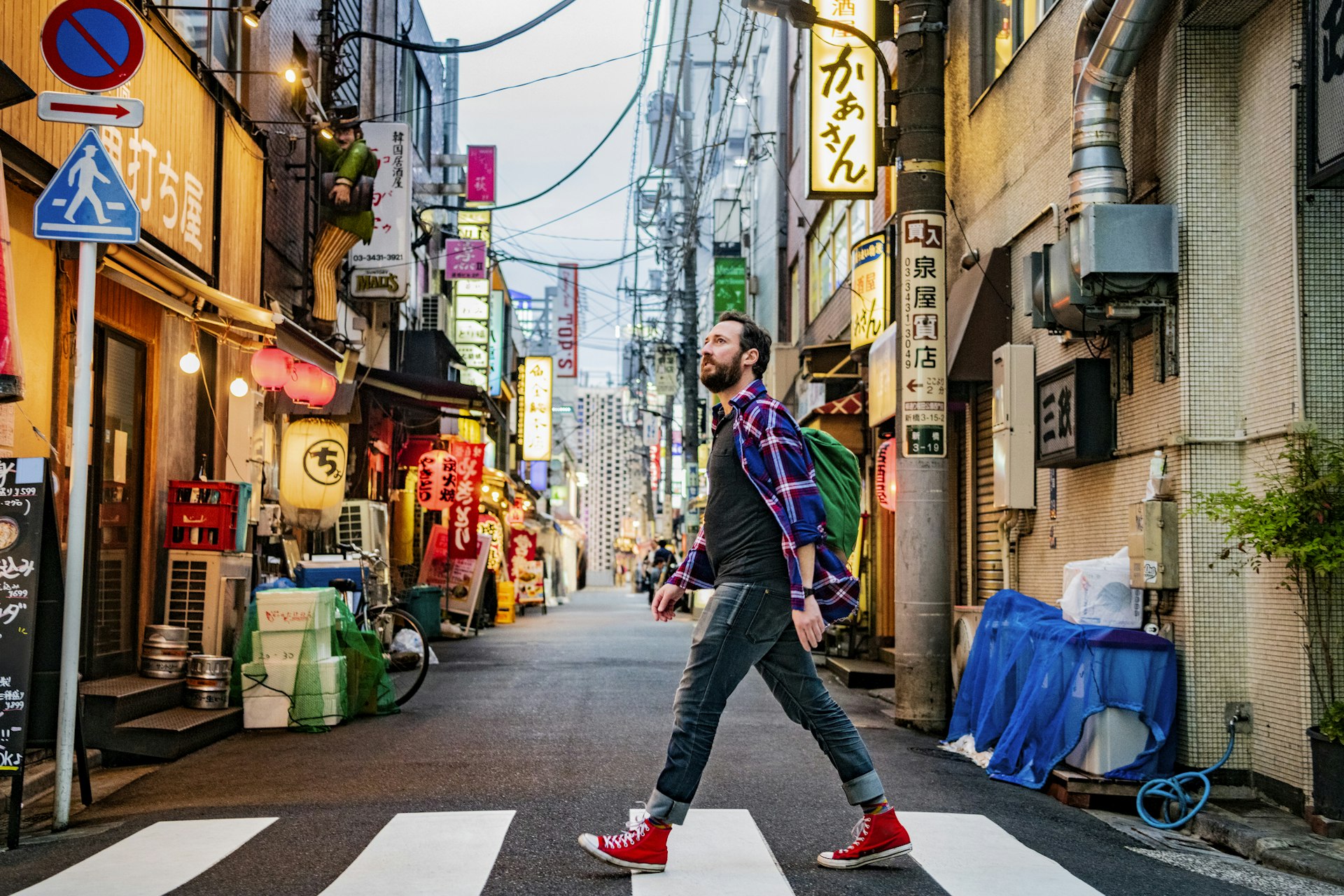 A white man walks across a Tokyo street lined with neon signs and paper lanterns